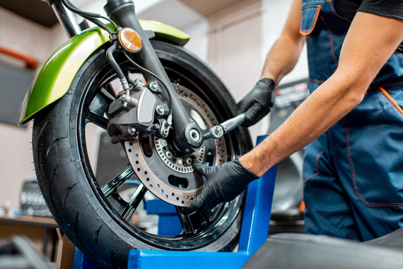 Immagine dell'officina Rinomotor's con un meccanico al lavoro sulla ruota anteriore della moto.